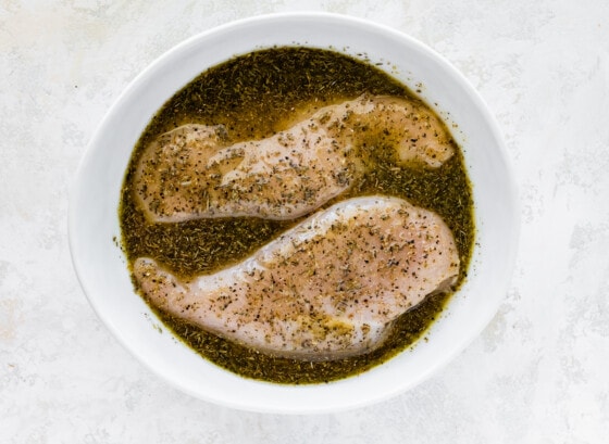 Two chicken breasts sitting in a white bowl of marinade.