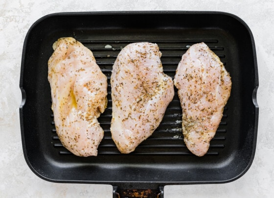 Three raw seasoned chicken breasts in a grill pan.