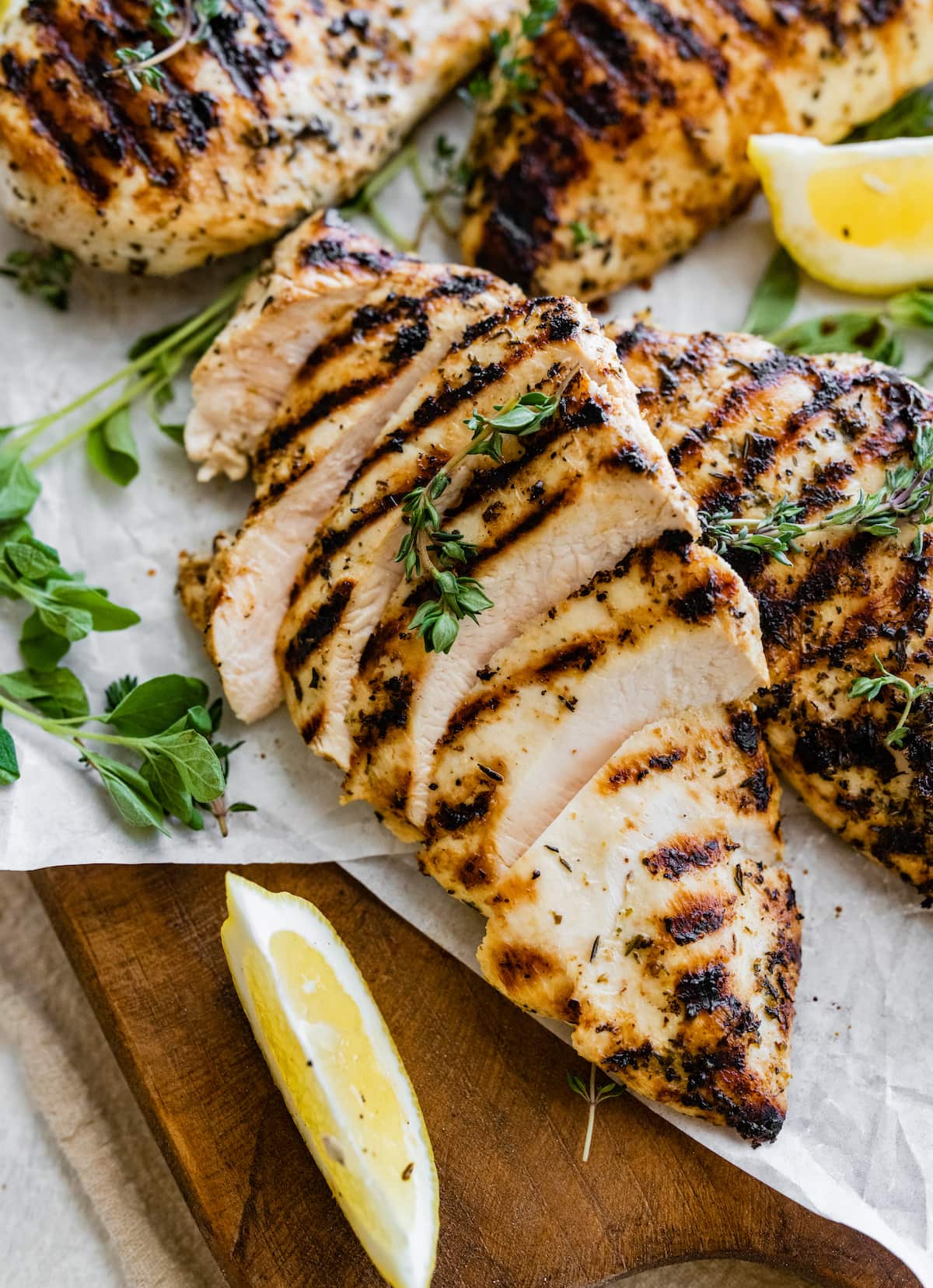 Sliced grilled chicken breast on a cutting board with fresh herbs and lemon slices.