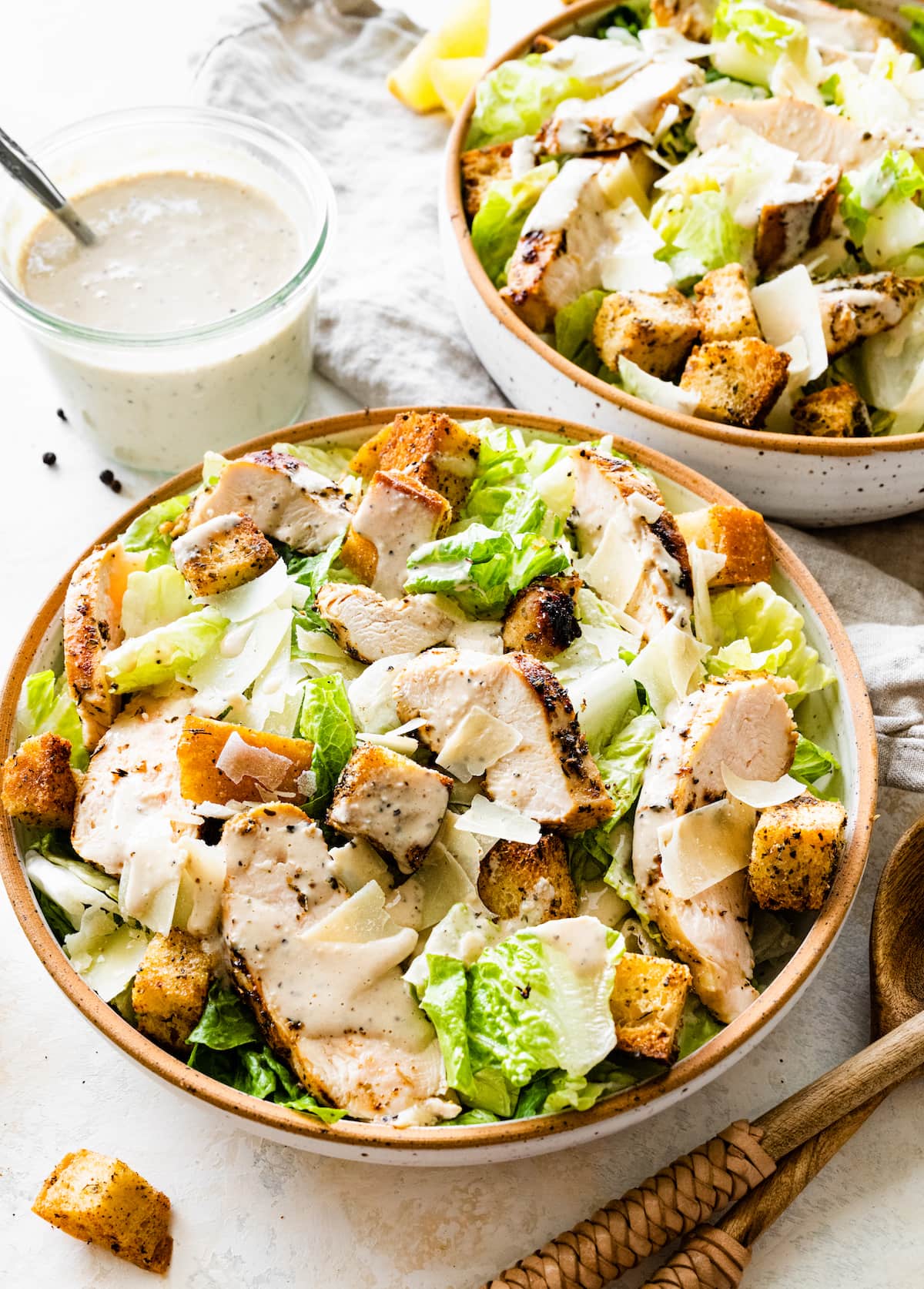 Grilled chicken Caesar salad in a bowl with two wooden serving spoons nearby.