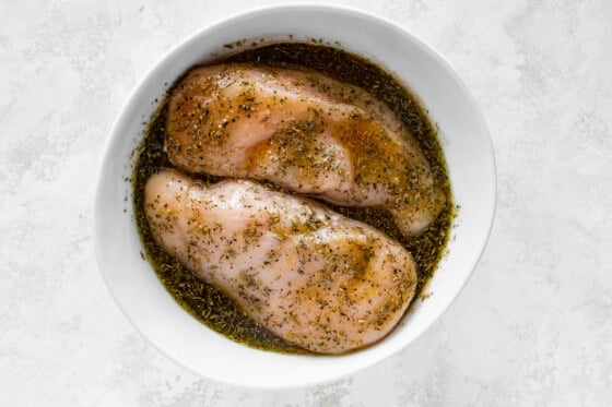 Two chicken breasts in a bowl of marinade.