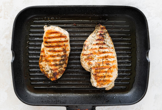 Two grilled chicken breasts on a grill pan.