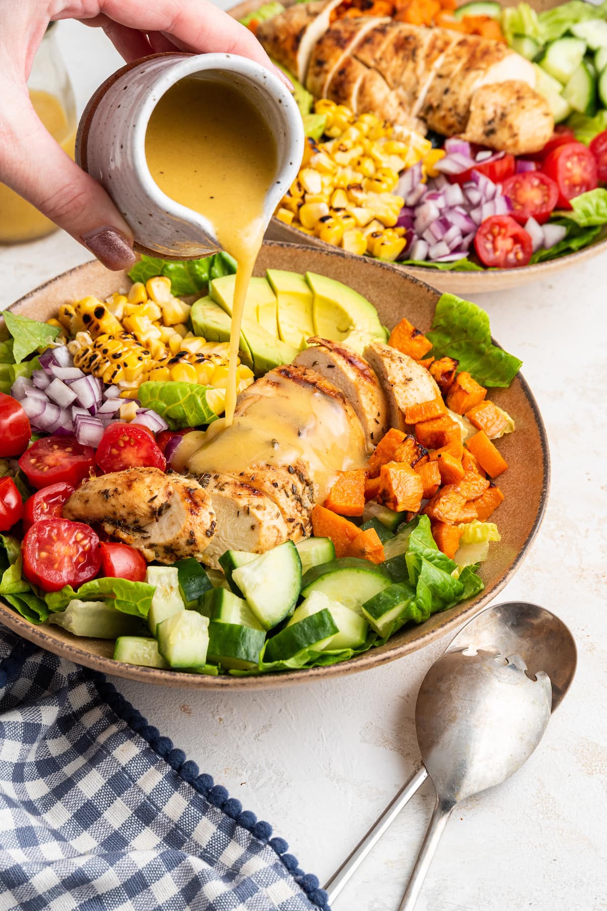 A woman's hand pouring dressing over a bowl of grilled chicken salad.