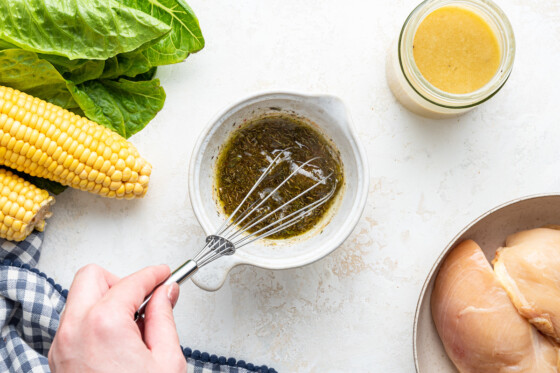 A woman's hand using a whisk in a bowl of marinade.