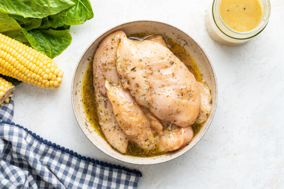 Raw chicken breasts in a bowl of marinade.