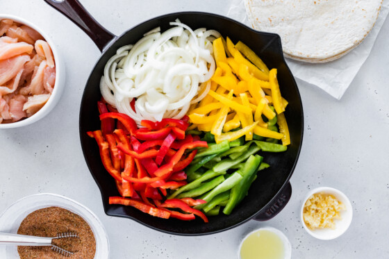 Raw bell peppers and onion in a cast iron skillet.