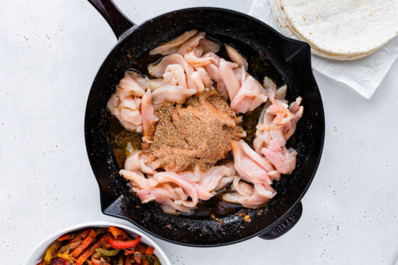 Seasonings and raw chicken in a cast iron skillet.