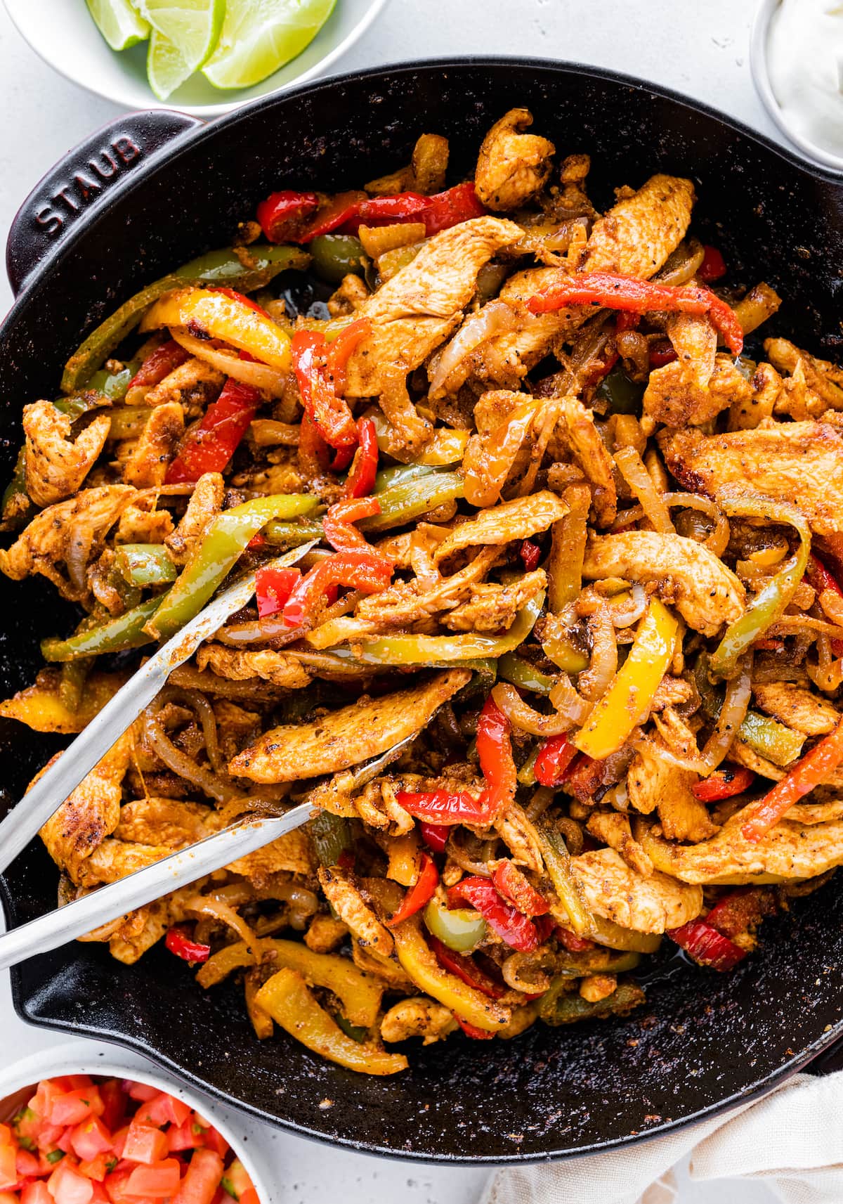 Chicken fajita mix in a cast iron skillet with metal tongs.