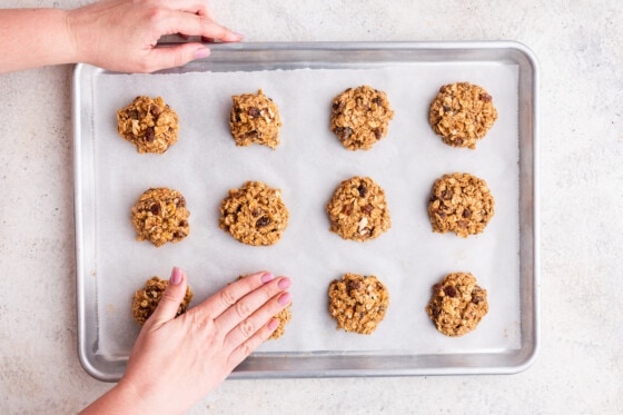A woman's hand pressing the oatmeal breakfast cookies to make a disc shape before being baked in the oven.