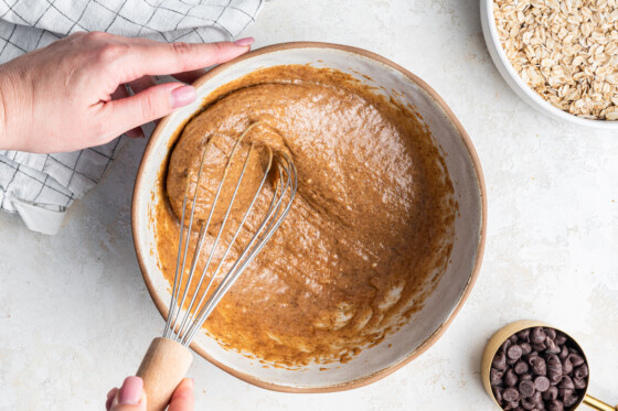 A woman's hand using a whisk in a bowl of wet ingredients for the healthy oatmeal chocolate chip bars.