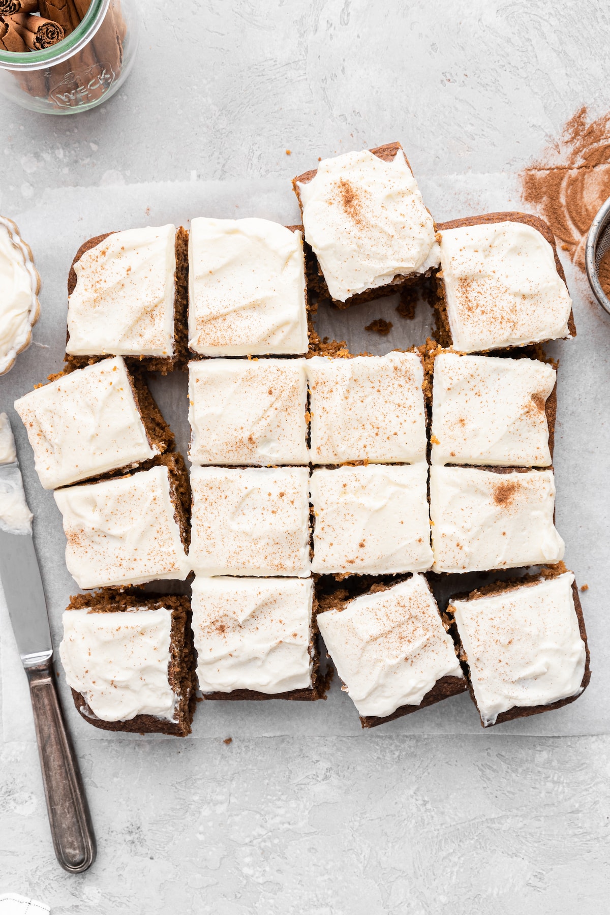 Pumpkin cake sliced into cube-shaped pieces topped with a cream cheese frosting on parchment paper.