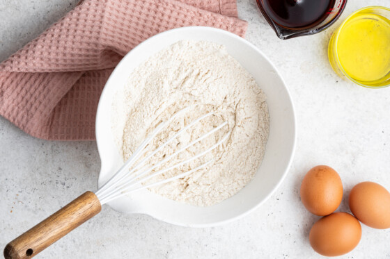 Flour in a white mixing bowl with a whisk.