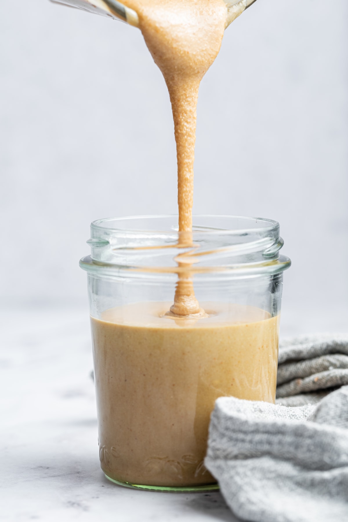 Tahini being poured into a glass jar.