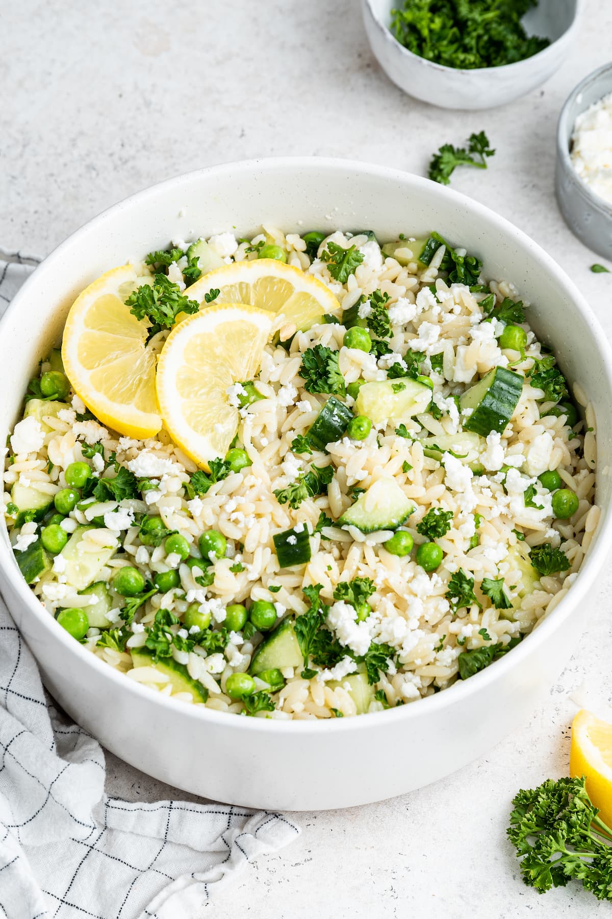 Lemon orzo salad with fresh lemon wedges in a white bowl.
