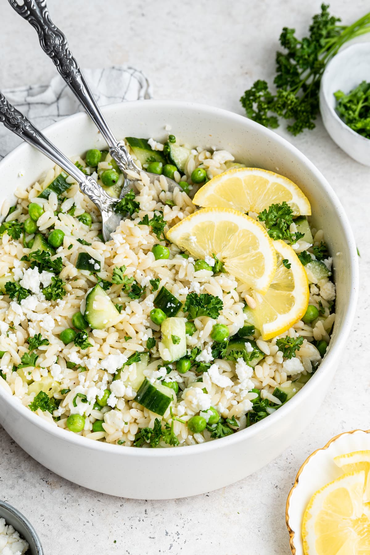 Lemon orzo salad with fresh lemon slices in a white bowl with metal serving spoons.