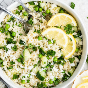 Lemon orzo salad with fresh lemon slices in a white bowl with metal serving spoons.