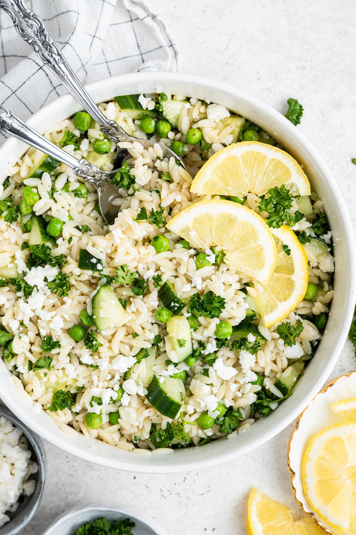 Lemon orzo salad with fresh lemon slices in a white bowl with metal serving spoons.