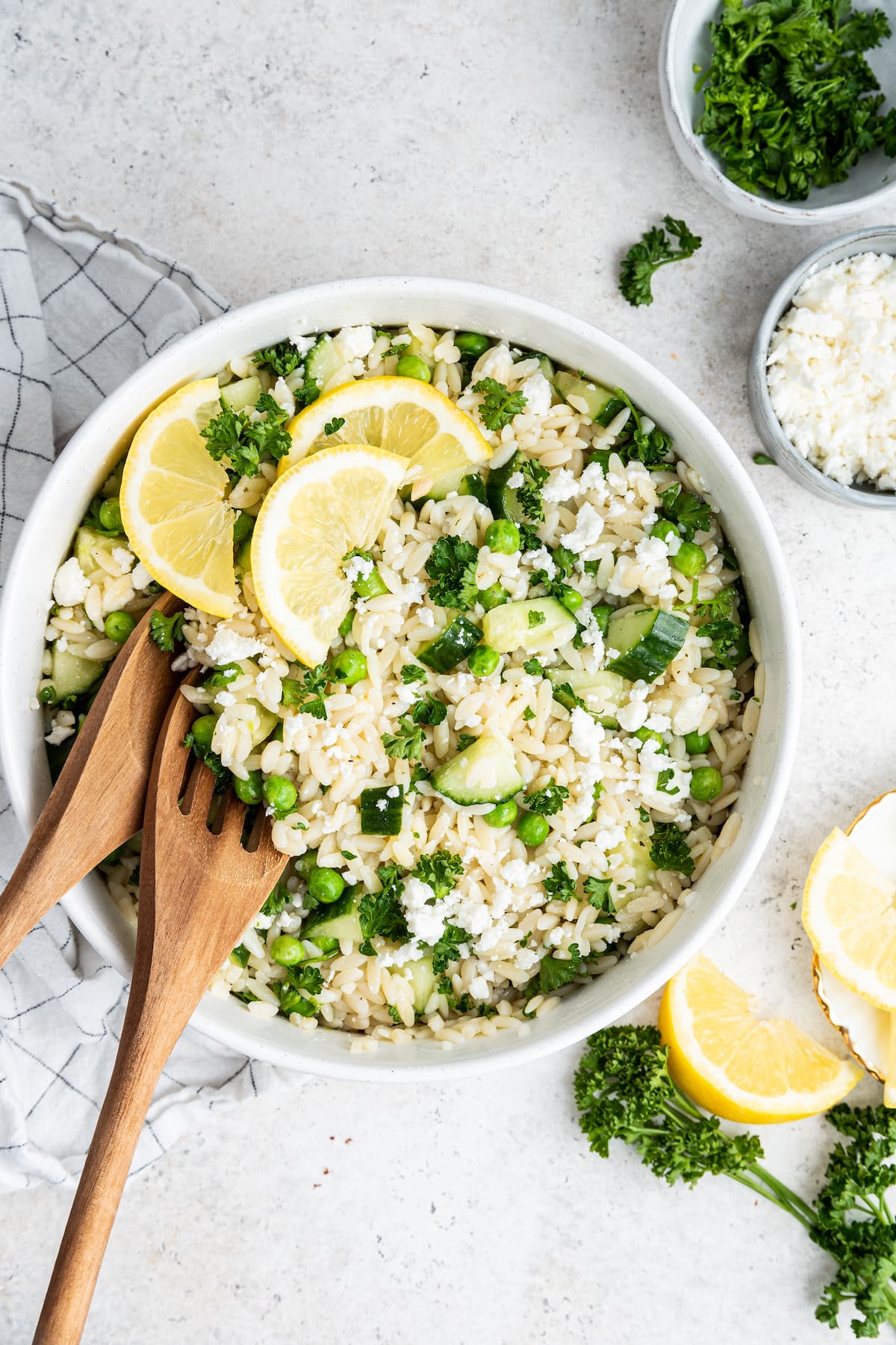 Lemon orzo salad with fresh lemon wedges in a white bowl with wooden serving spoons.