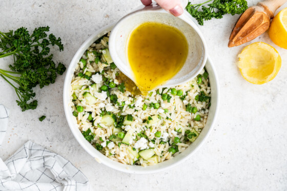 A woman's hand pouring a dressing over the lemon orzo salad.