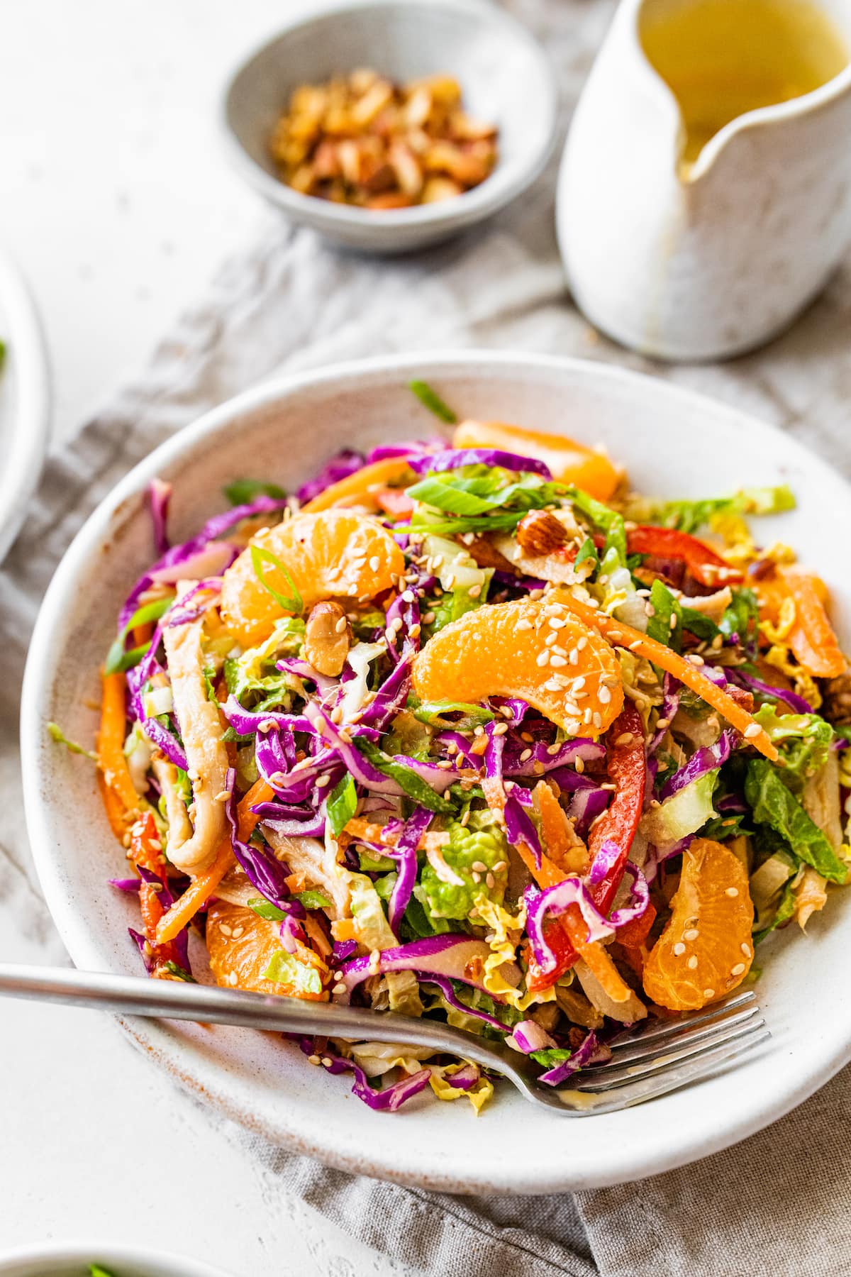 Mandarin orange chicken salad in a shallow white bowl with a metal fork.