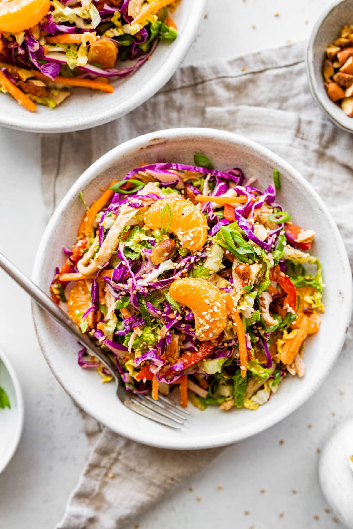 Mandarin orange chicken salad in a shallow white bowl with a metal fork.