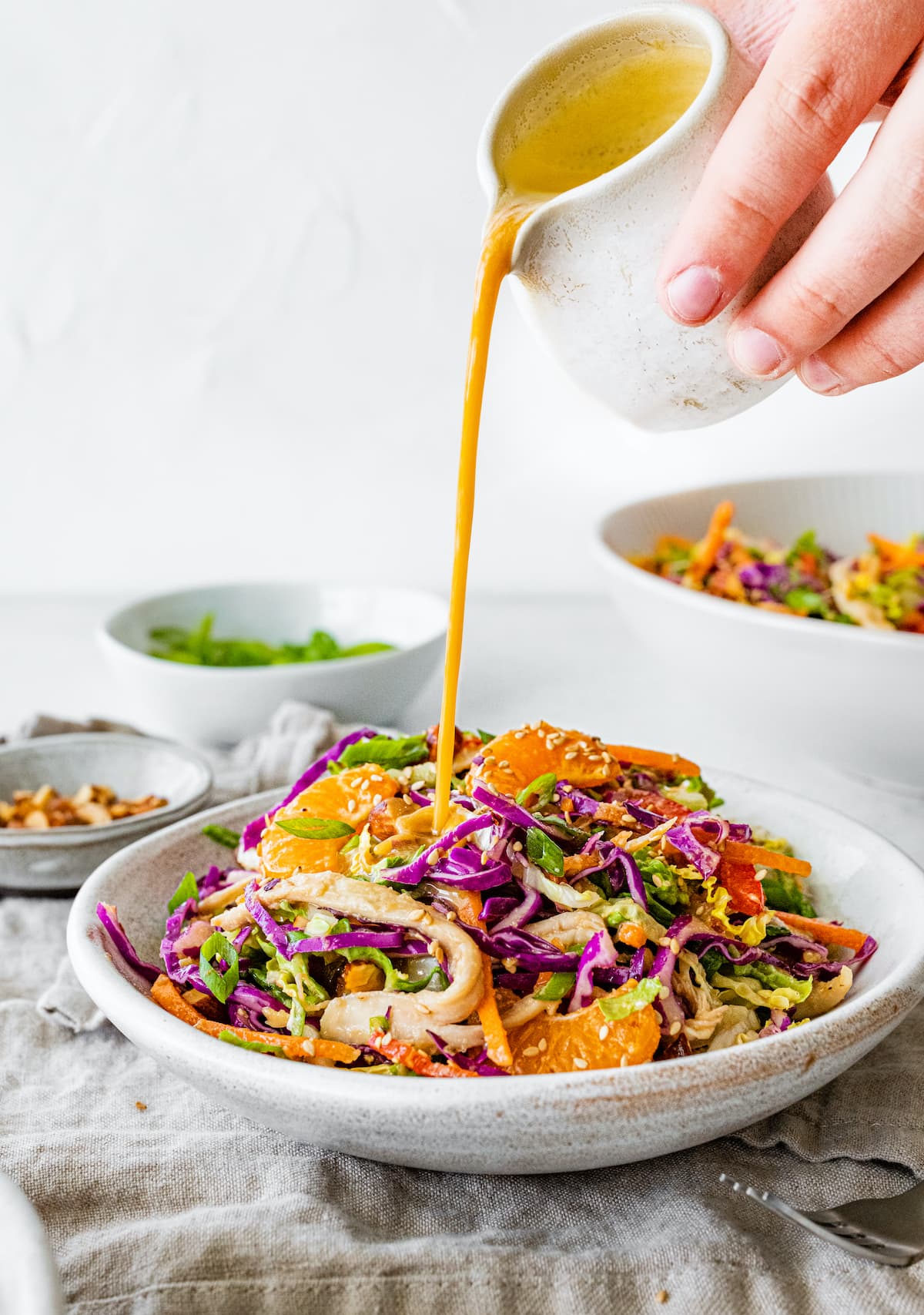 A woman's hand pouring dressing over a mandarin orange chicken salad shallow white bowl.