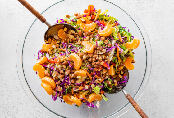 Mandarin orange chicken salad in a large glass bowl with two serving spoons.