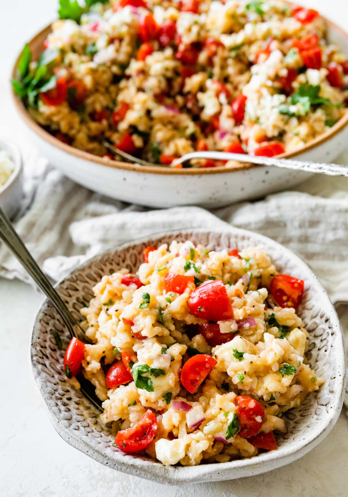 A small bowl of Mediterranean brown rice salad near a larger bowl with the same salad.