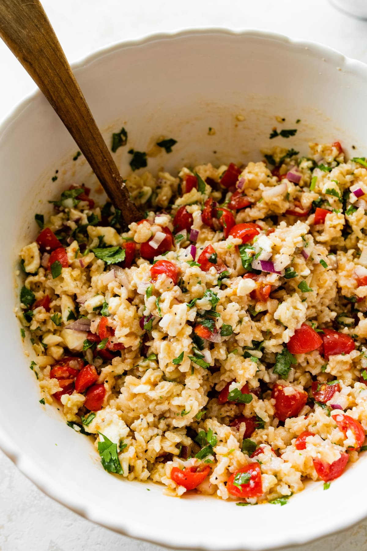 Mediterranean brown rice salad in a large white mixing bowl with a wooden spoon.