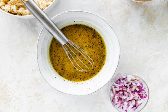 A salad dressing in a white bowl with a metal whisk.