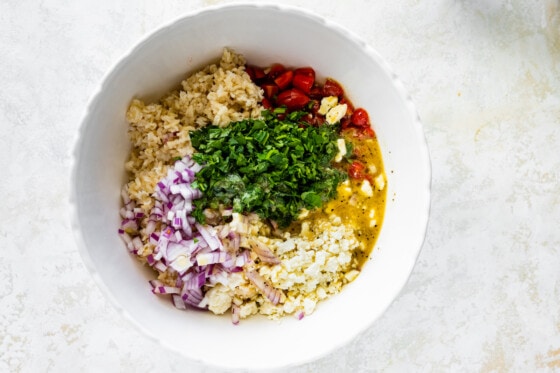 Ingredients for the Mediterranean brown rice salad in a large white bowl.