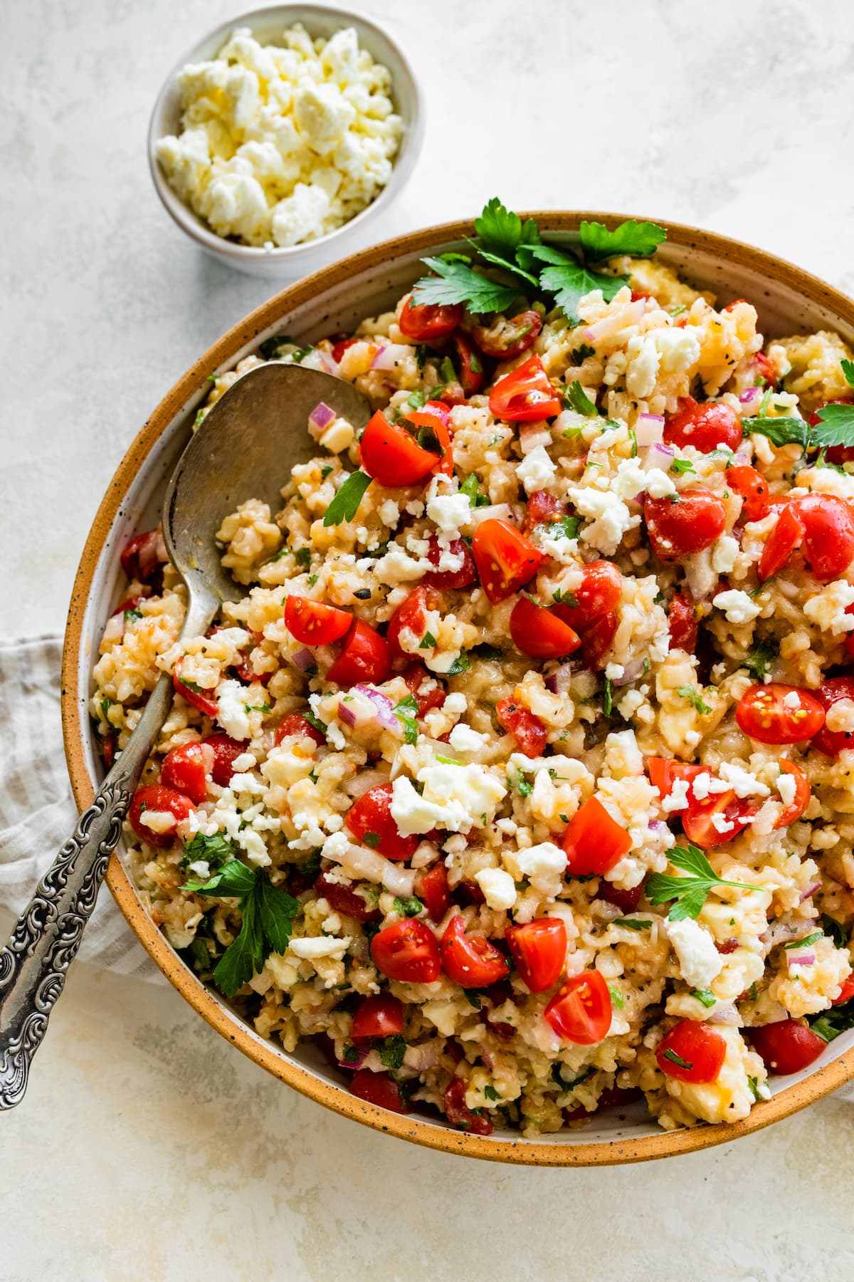 Mediterranean brown rice salad in a bowl with a metal serving spoon.