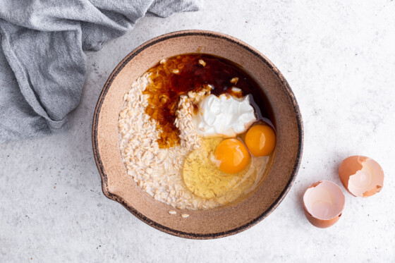 Ingredients for the overnight oatmeal oats in a large mixing bowl. These include eggs, yogurt, maple syrup, oats, and milk.