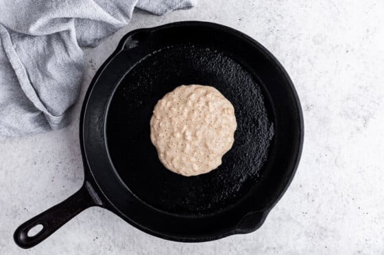 An overnight oatmeal pancake is made in a cast iron skillet. The top has formed tiny bubbles.