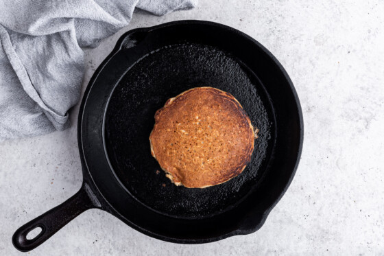 A complete overnight oatmeal pancake with a slightly crisp brown top in a cast iron skillet.