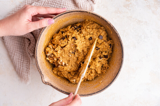 A woman's hand with a silicone spatula used to mix the dough in a large mixing bowl for the pumpkin oatmeal bars.