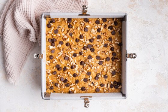 Pumpkin oatmeal bars before being baked in a square baking dish topped with chocolate chips and crushed walnuts.