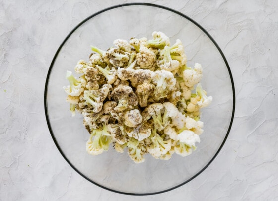 Cauliflower florets in a large glass bowl with seasonings.