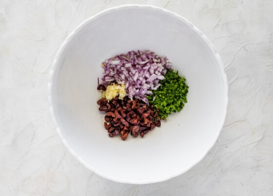 Red onion, garlic, olives, and parsley in a large white bowl.