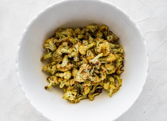 Roasted cauliflower in a large bowl with olive oil, herbs, and spices.