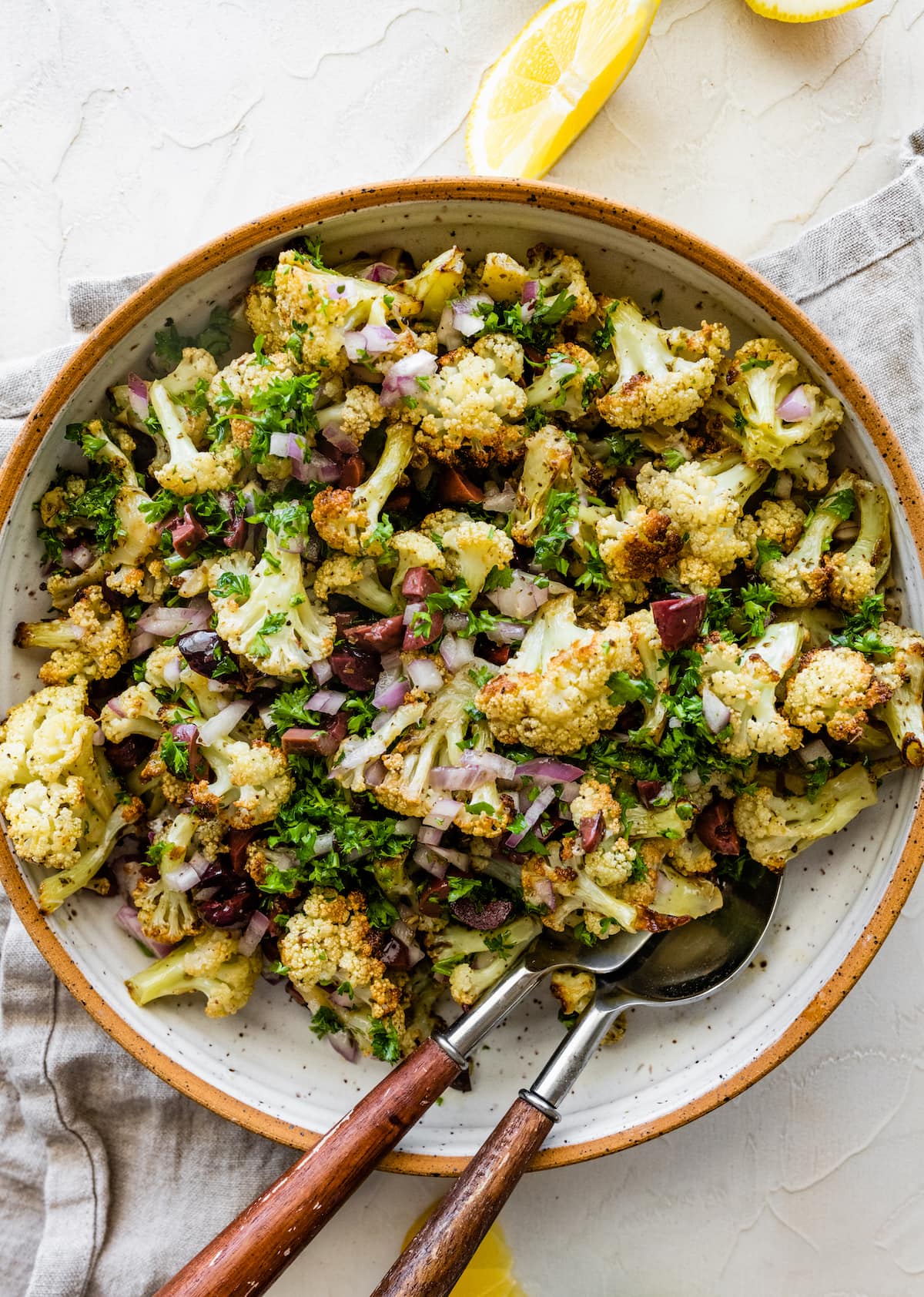 Roasted cauliflower salad in a large bowl with serving spoons.