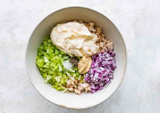Ingredients for the rotisserie chicken salad in a large bowl. Noticeable ingredients are chicken, red onion, celery, mayo, mustard, salt, and pepper.