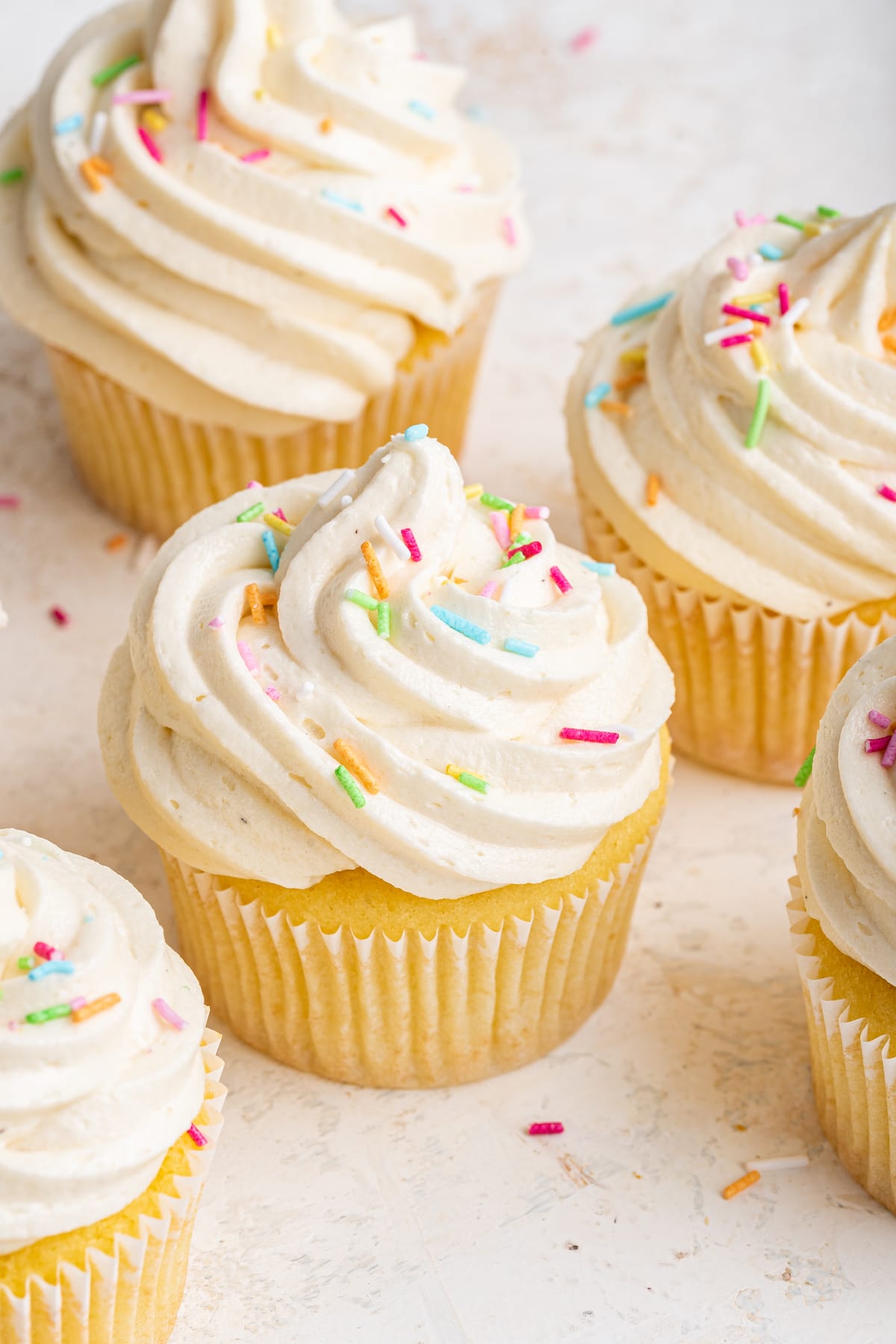 Multiple cupcakes with vanilla buttercream frosting and sprinkles.