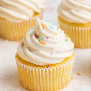 A cupcake with vanilla buttercream frosting and sprinkles on top.