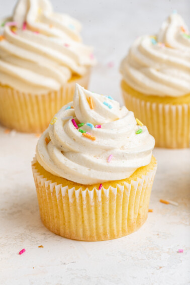 A cupcake with vanilla buttercream frosting and sprinkles on top.