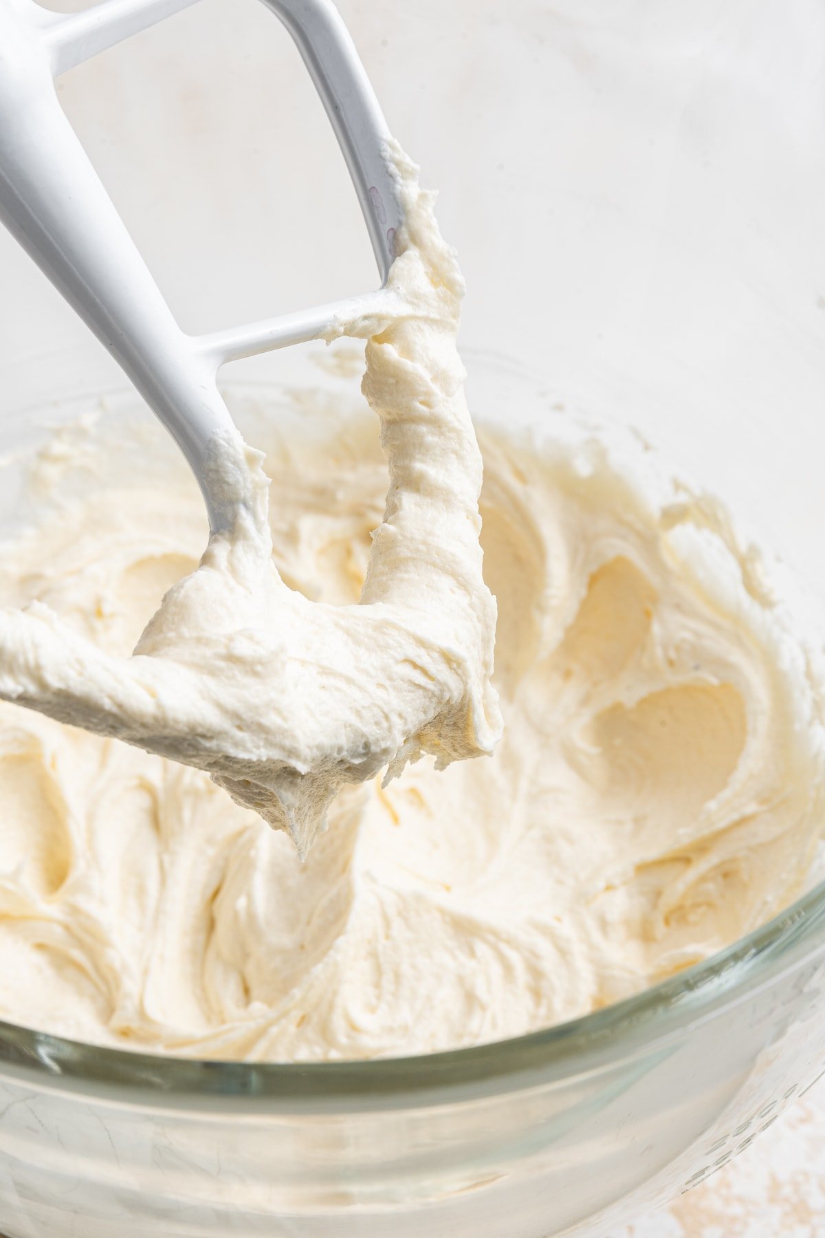 A flat beater in a bowl of vanilla buttercream frosting.