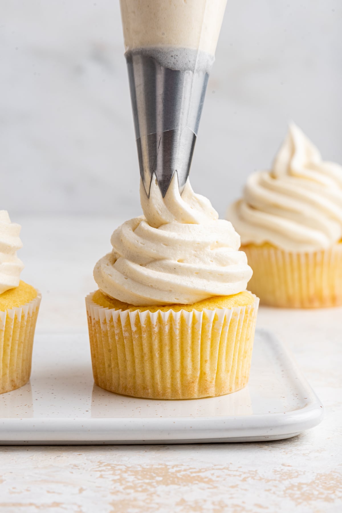 A pastry bag adding vanilla buttercream frosting to a cupcake.