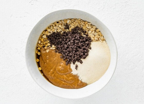 A large bowl of ingredients for vegan protein balls, including chocolate chips, oats, almond butter, and protein powder.