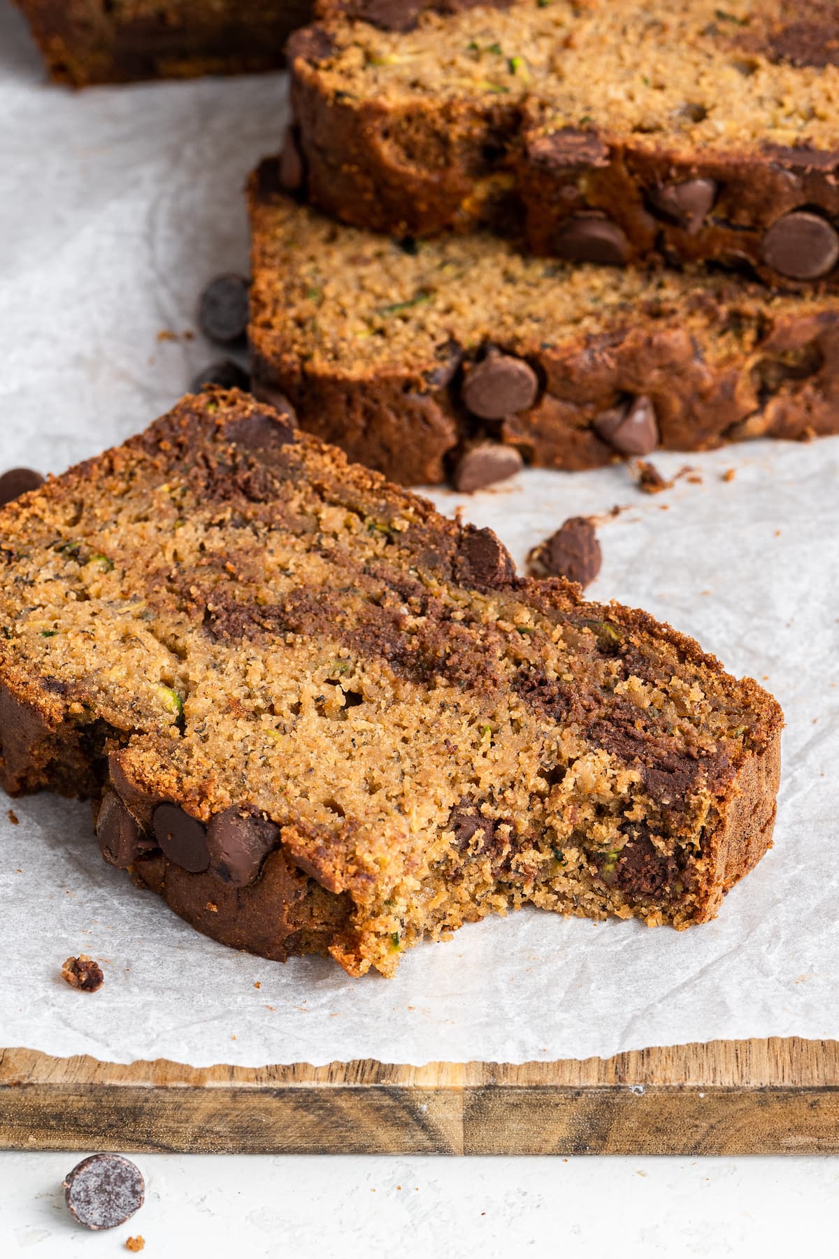 A slice of zucchini banana bread on a wooden cutting board with a bite taken out of it.