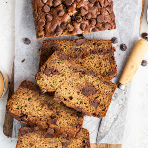 A loaf of zucchini banana bread on a wooden cutting board with four slices cut from it.